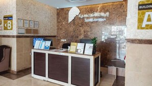 En receptionsdisk med informationsskärmar, en väggmonterad skylt och en växt.