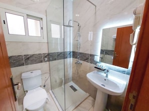 A bathroom with a glass-enclosed shower, a white toilet, and a sink with a mirror. - Iwan Alandalusia Hotel Suites Alrehab (Jeddah)