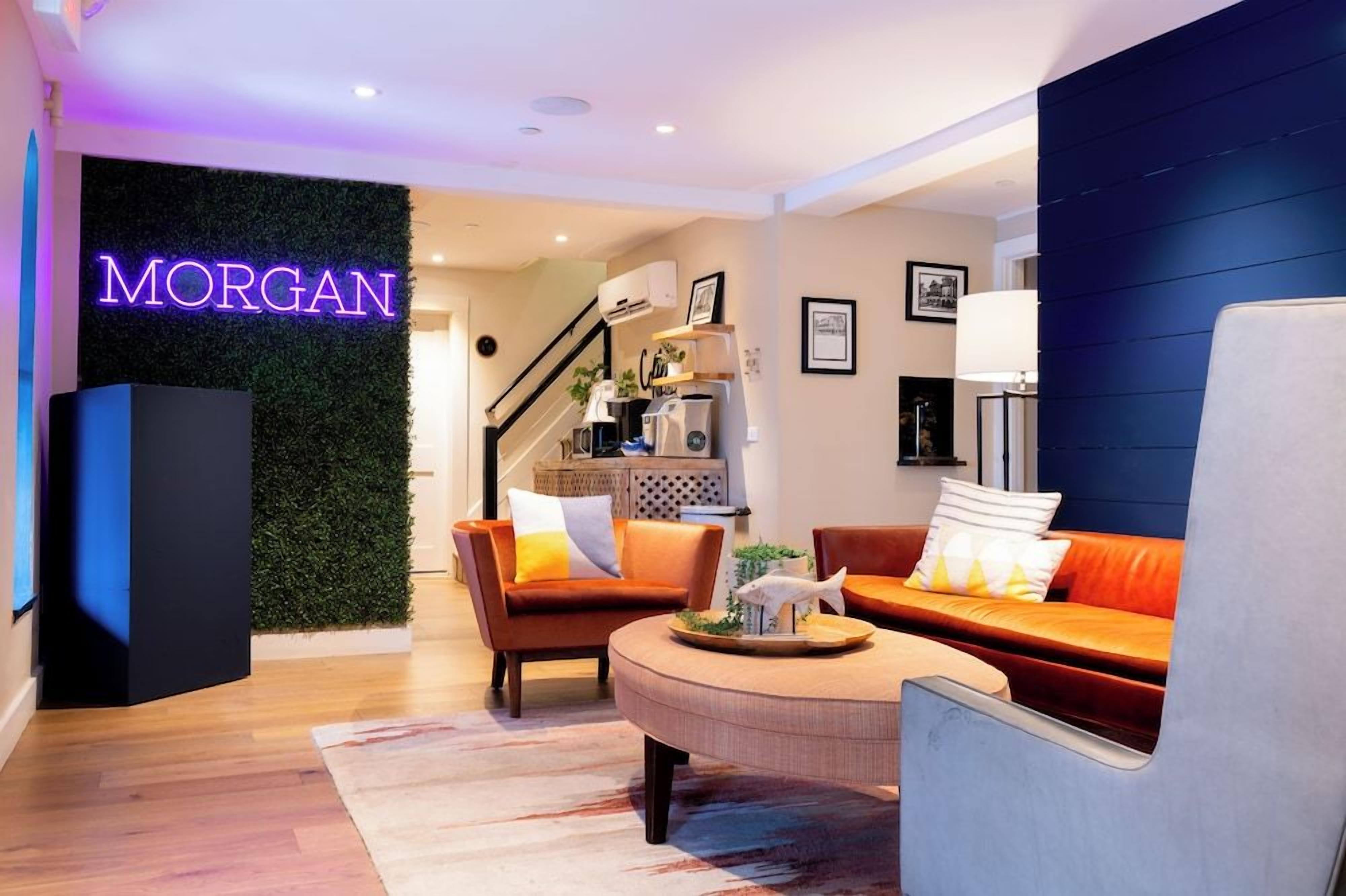 A modern hotel lobby with a neon sign, a staircase, seating area, and a reception desk.