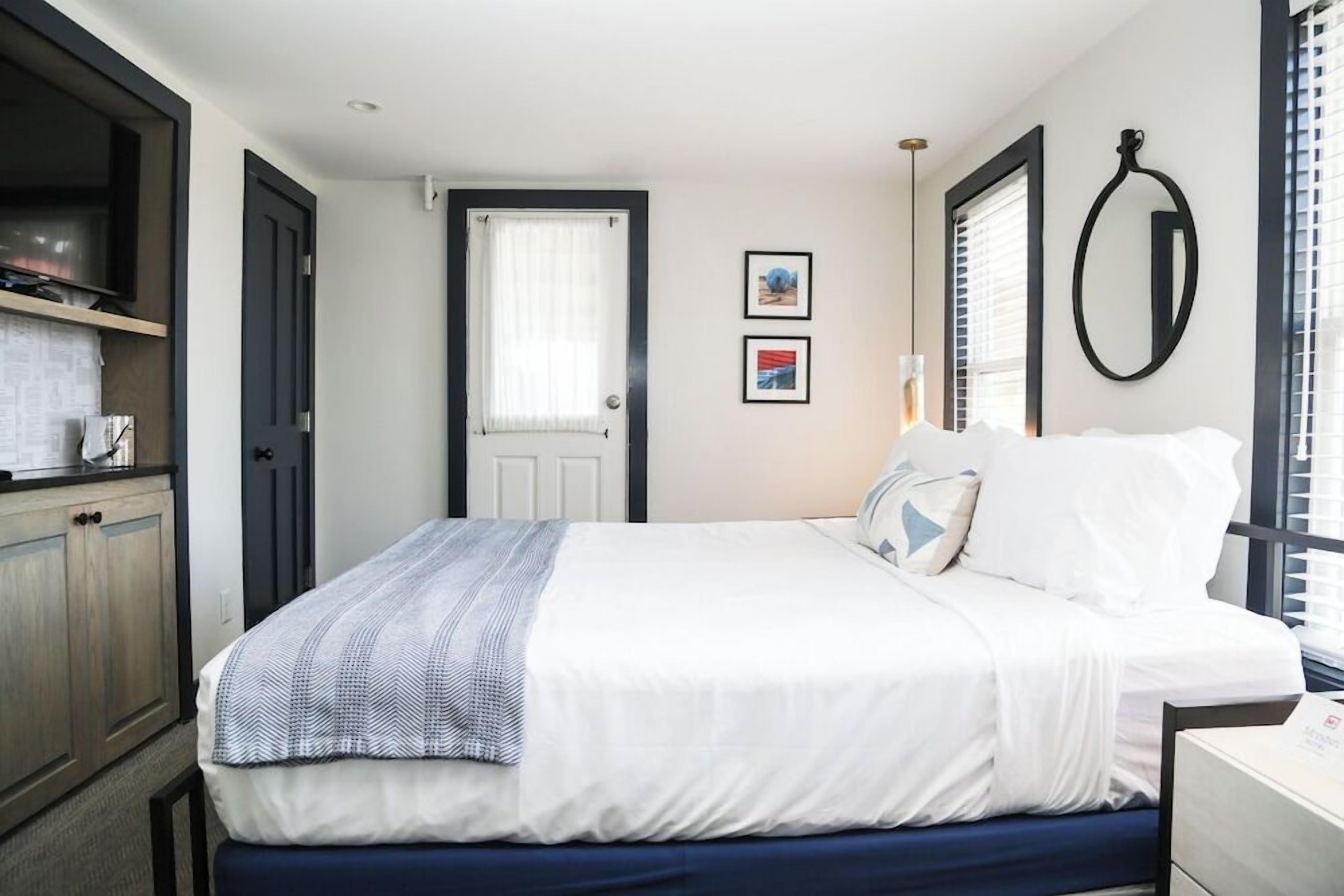 A bedroom with a bed, a door, a window with blinds, and a wall-mounted mirror.