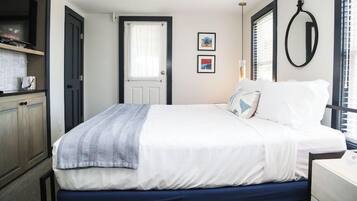 A bedroom with a bed, a door, a window with blinds, and a wall-mounted mirror.