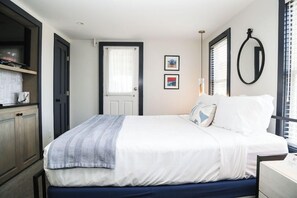 A bedroom with a bed, a door, a window with blinds, and a wall-mounted mirror. - Hotel Ginger (Oak Bluffs)