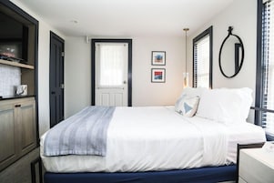 Un dormitorio con cama, puerta, ventana con persianas y espejo adosado a la pared.