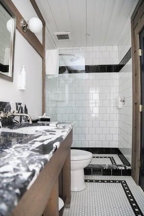 Et badeværelse med kommode i marmor, toilet, bruser og flisegulv.