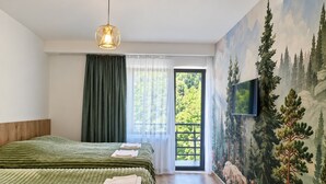 Quarto com duas camas, uma janela grande com cortinas, um quadro de árvores e uma televisão na parede.