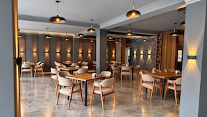 Interior moderno de restaurante com várias mesas e cadeiras, luminárias pendentes e painéis decorativos na parede.