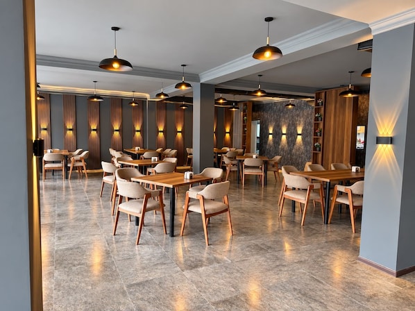 A modern restaurant interior with multiple dining tables and chairs, pendant lighting, and decorative wall panels.