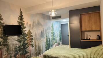A bedroom with a forest mural, a bed with a striped bedspread, a flat-screen TV, a wooden cabinet, and a pendant light.
