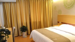 Une chambre d’hôtel avec un lit, des rideaux, une plante en pot et une tête de lit en bois.