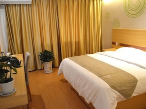 Ein Hotelzimmer mit Bett, Vorhängen, einer Topfpflanze und einem hölzernen Kopfteil.