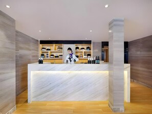 A reception desk with a marble top, wooden flooring, and shelves with various items. - Kyriad Marvelous Hotel Haerbin West High-speed Railway Station Wanda (Harbin)