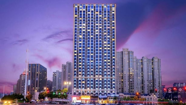 A high-rise building with multiple floors, surrounded by other tall buildings, and a busy intersection with traffic lights. - Kyriad Marvelous Hotel Haerbin West High-speed Railway Station Wanda (Harbin)