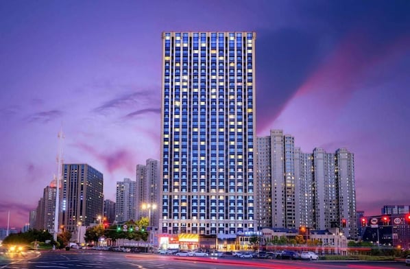 A high-rise building with multiple floors, surrounded by other tall buildings, and a busy intersection with traffic lights. - Kyriad Marvelous Hotel Haerbin West High-speed Railway Station Wanda (Harbin)