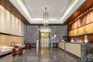 Eine Hotelhalle mit einer Rezeption, einer Lounge und einem modernen Kronleuchter.