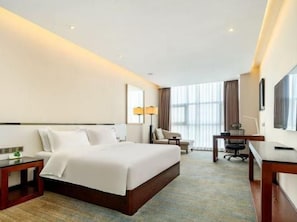 Ein Hotelzimmer mit einem großen Bett, einem Schreibtisch, einem Stuhl und einem Fernseher.