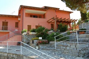 Um edifício de vários andares com escadaria de pedra, pérgula de madeira e varanda.