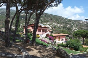 Eine rosa Villa mit einem Kiesweg, umgeben von Bäumen und einem Bergpanorama.
