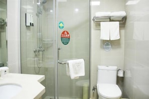 Um banheiro com chuveiro em gabinete de vidro, vaso sanitário e pia. Toalhas penduradas em um suporte e um dispensador de sabonete na parede.