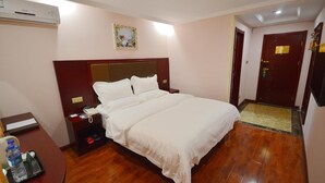 A hotel room with a large bed, a bedside table with a phone, a water bottle, and a small table with a tray. - Greentree Inn Nantong Qidong Lvsi Harbour Express Hotel (Nantong)