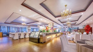 A spacious banquet hall with a central buffet area, multiple tables set for dining, and a large window providing natural light. - Rezen Hotel (Linyi)