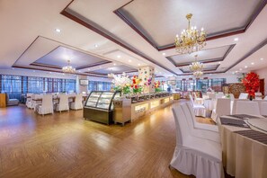 A spacious banquet hall with a central buffet area, multiple tables set for dining, and a large window providing natural light. - Rezen Hotel (Linyi)