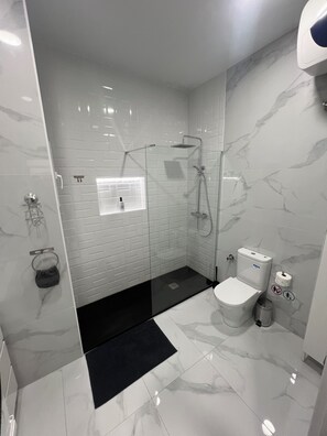 Uma casa de banho moderna com chuveiro separado por vidro, sanita e bidé.