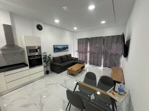 Eine moderne Küche mit Einbauofen und Mikrowelle, ein Essbereich mit Glastisch und Stühlen, eine Sitzecke und ein an der Wand montierter Fernseher.