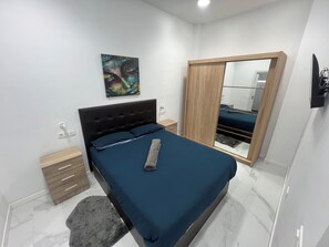 Ein Schlafzimmer mit einem Bett, einem Nachttisch, einem Holzschrank, einem Spiegel und einem Bild an der Wand.