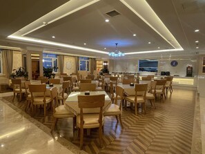 A spacious dining area with multiple tables and chairs, a chandelier, and a reception desk. - Vienna International Hotel (Ürümqi)
