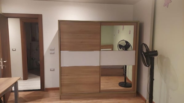 Una habitación con un armario de madera, un ventilador y una puerta que da a otra habitación.