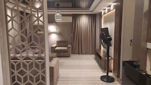 Una habitación de hotel moderna con sofá, mueble para televisor, separador decorativo y ventilador de techo.