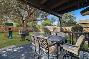 An outdoor patio with a table and chairs, a barbecue grill, and a wooden deck.