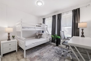 A room with a bunk bed, desk, chair, lamp, and a potted plant.
