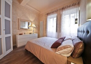 Un dormitorio con cama, cómoda, espejo y ventana con cortinas.