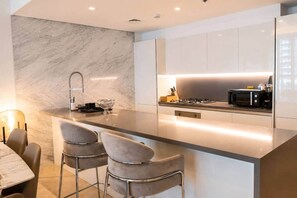A modern kitchen with a marble backsplash, stainless steel appliances, and a bar area with two stools. - New 1BR in Business Bay  Free Padel Court, Pool, Sauna (Dubai)