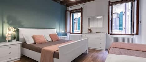 Un dormitorio con cama, mesitas de noche, cómoda y ventana con contraventanas.