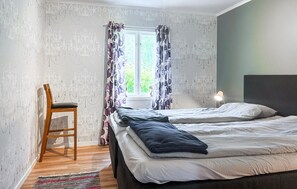 Ein Schlafzimmer mit einem Bett, einem Sessel, einem Fenster mit Vorhängen und einem Nachttisch mit Lampe.