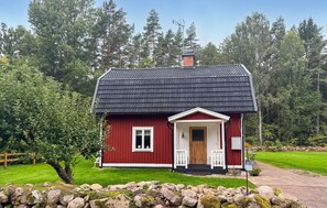 Ein rotes Holzhaus mit dunklem Dach, weißer Tür und einer kleinen Veranda.