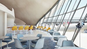 Un interior moderno con mesas y sillas redondas, ventanas amplias y vista al aeropuerto.