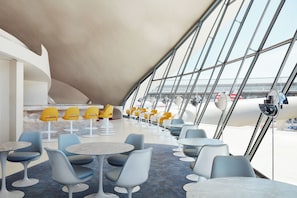 A modern interior with round tables and chairs, large windows, and a view of the airport. - TWA Hotel (Jamaica)