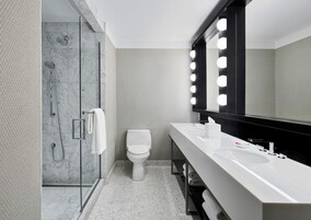 Un baño moderno con ducha envuelta en vidrio, inodoro blanco y tocador con un espejo grande e iluminación.