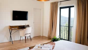 Una habitación de hotel con cama, escritorio, silla, televisor y balcón con cortinas.