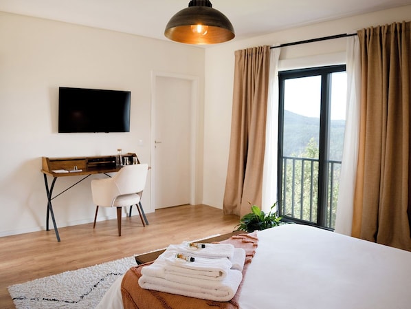 A hotel room with a bed, a desk, a chair, a television, and a balcony with curtains.