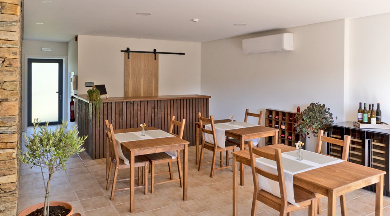 Un restaurante con mesas y sillas de madera, una zona de bar con botellas de vino y una pequeña planta en maceta.