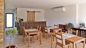 Un restaurante con mesas y sillas de madera, una zona de bar con botellas de vino y una pequeña planta en maceta.