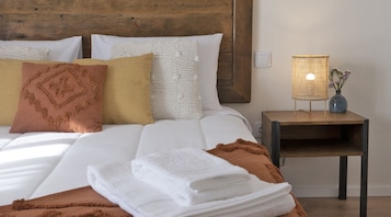 Una cama bien hecha con ropa de cama blanca y marrón, una mesita de noche con una lámpara y un florero con flores.