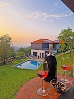 Vista de la piscina con una casa, una botella de vino y copas sobre una mesa.