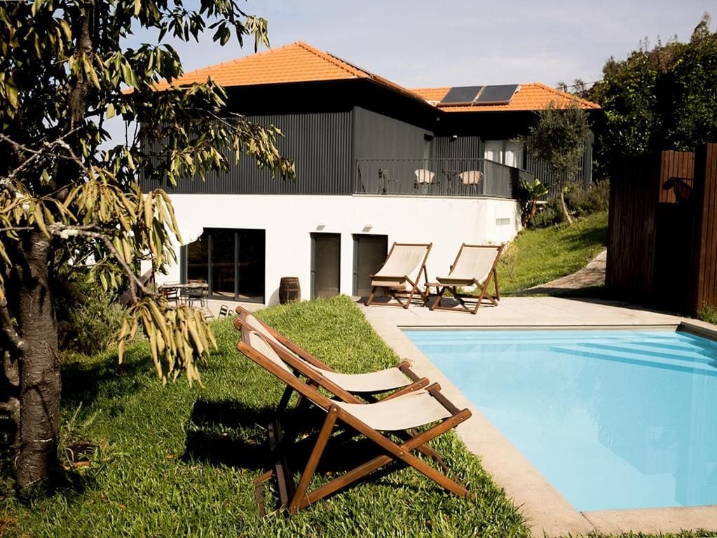 Una casa moderna con piscina, mobiliario exterior y un árbol.