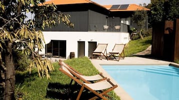 Una casa moderna con piscina, mobiliario exterior y un árbol.