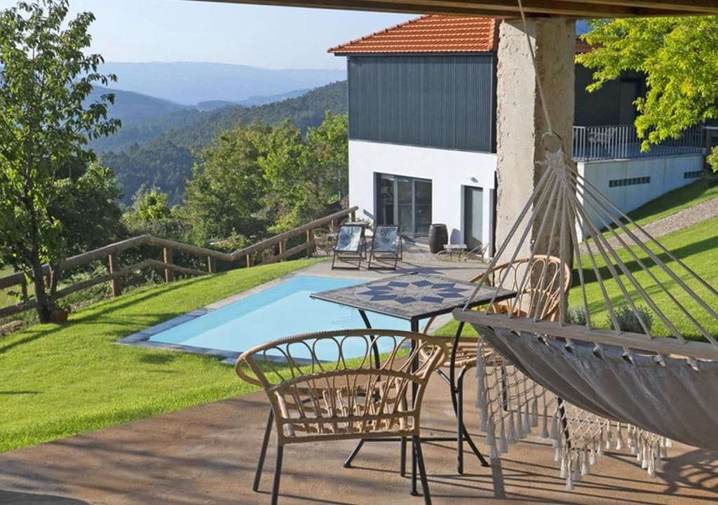 Zona de piscina con mobiliario exterior y una hamaca, con vistas a un paisaje montañoso.